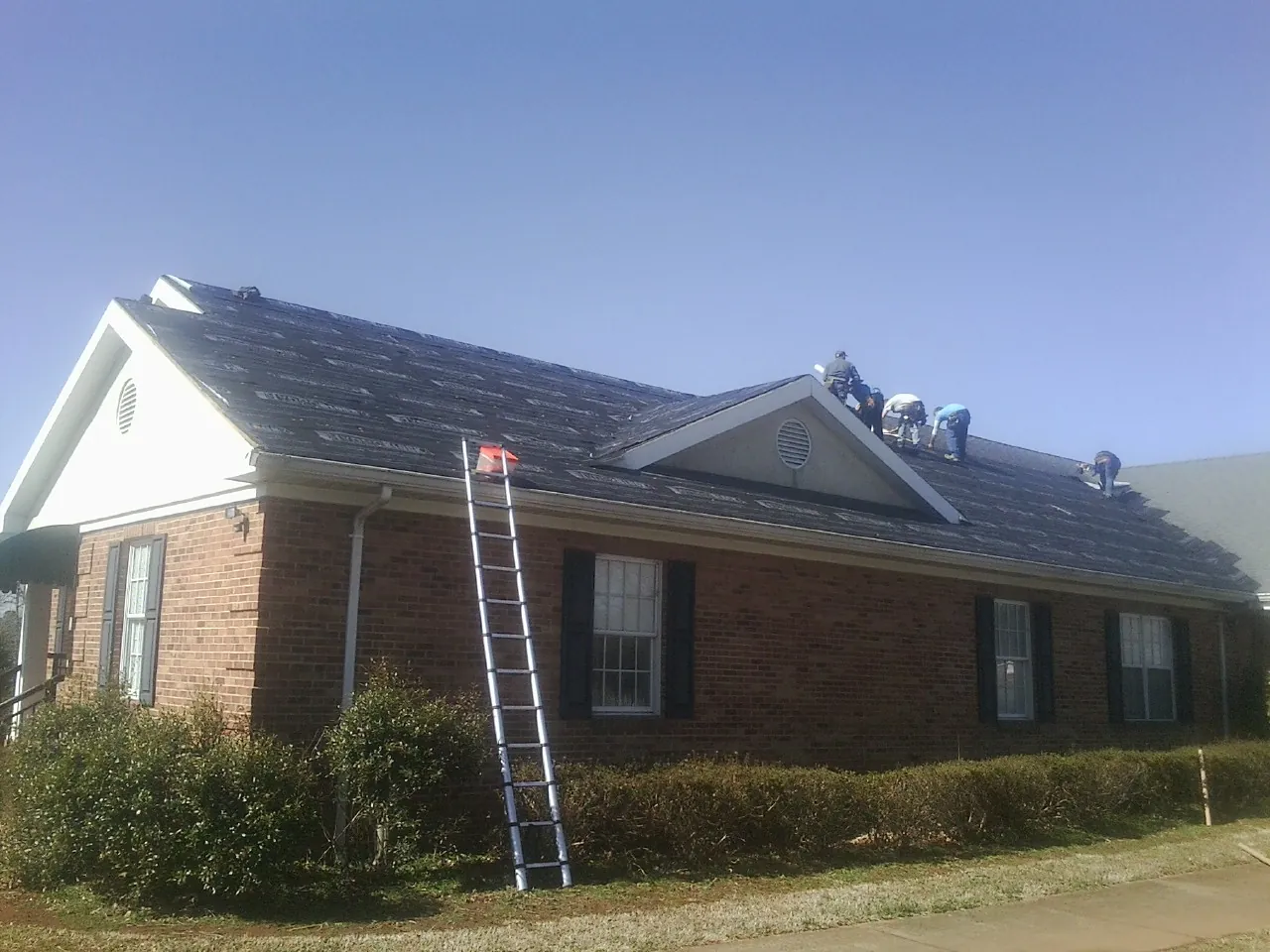 Crew tearing shingles off a brick ranch roof with a ladder set — Emergency Roof Repair work by our crew in Peebles
