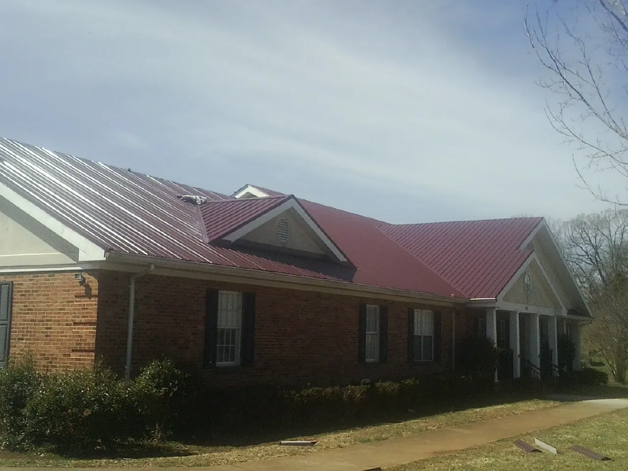 Red metal roof with gabled entries on a long brick building, from a Hail Damage Roof Repair job in Peebles