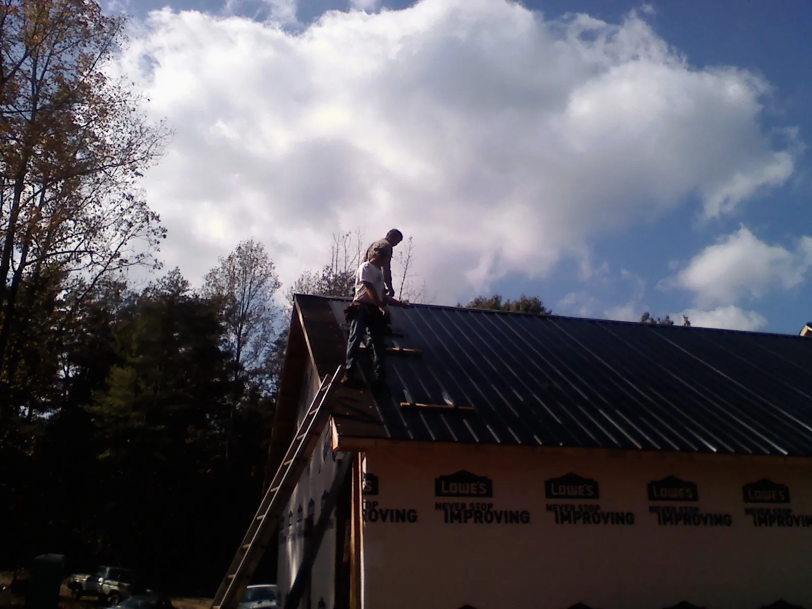 Roofer fastening dark metal panels high against a cloudy sky, from a Roof Inspection job in Peebles